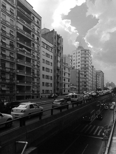 Foto em preto e branco de avenida com prédios altos e trânsito